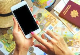 Hands holding smart phone with Euro money banknotes bills as travel passport on copy space background. Travelling light, comfortable journey concept.